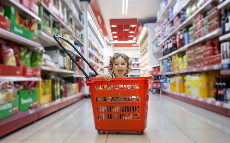 Egy gyerek ül egy bevásárlókosárban a boltban.