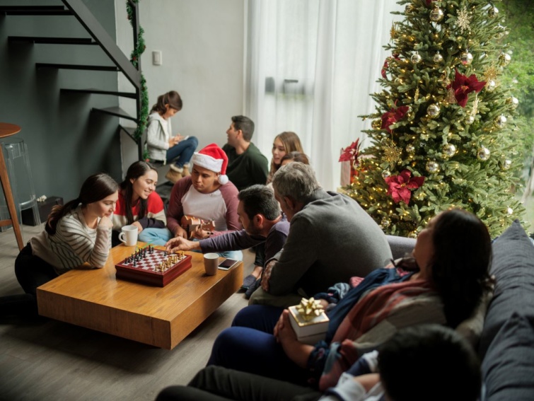 Egy család a karácsonyfa előtt közösen sakkozik.