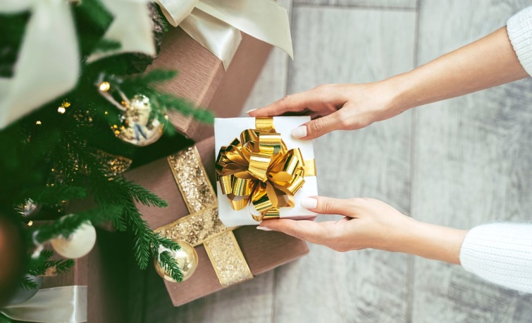 Egy női kéz ajándékot helyez a karácsonyfa alá.