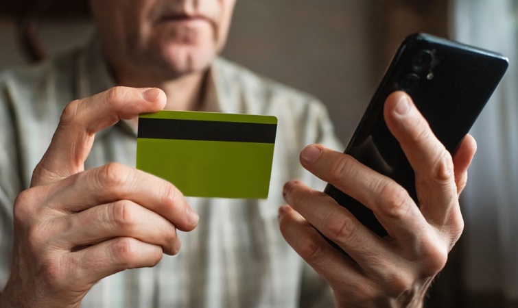 ferfibankkartyamobiltelefon Startlap Vásárlás Egy férfi egy bankkártyát és egy mobiltelefont tart a kezében.
