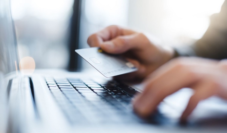 Egy ember egyik kezében bankkártya, a másikkal gépel egy billentyűzeten.