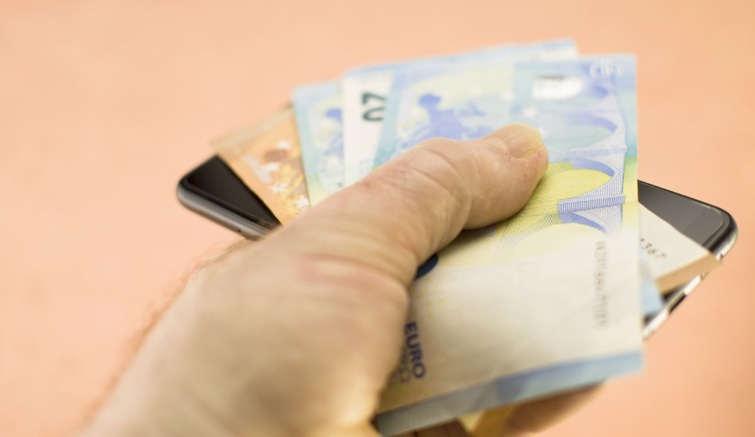 Egy kéz euróbankjegyeket és egy mobiltelefont tart.