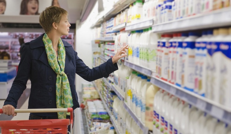 Egy bevásárlókocsit toló nő a tejtermékeket nézi a boltban.