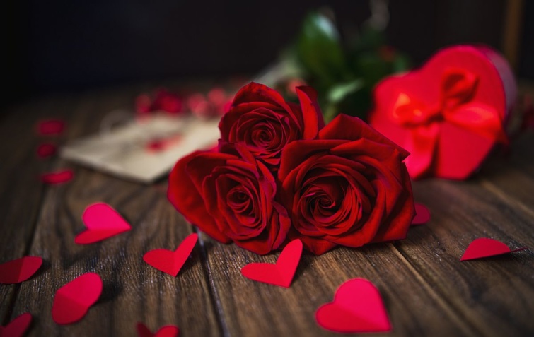 Papír szívecskék és egy csokor vörös rózsa az asztalon.
