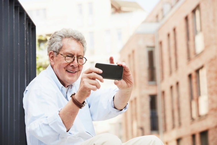 Idős férfi fotózik a telefonjával
