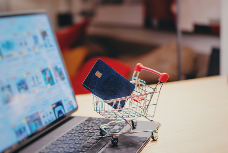 Mini bevásárlókosár bankkártyával laptop előtt egy íróasztalon