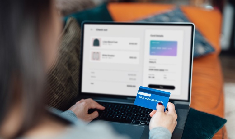 bankkartyalaptopmo Startlap Vásárlás Egy nő bankkártyával online vásárol, ölében egy laptop.
