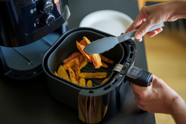 Air fryer, azaz forrólevegős sütőből vesz ki sült krumplit egy ember