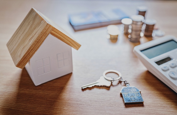 Lakáskulcs és kis házikó egy számológép mellett