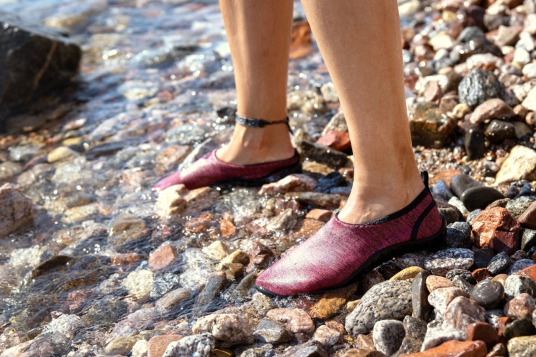 Nő vízicipőben a kavicsos vízparton