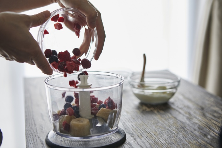 Női kéz gyümölcsöket helyez egy konyhai aprítóba barna konyhaasztalon