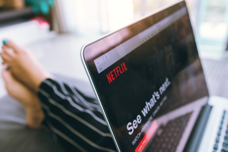 A Netflix kezdőképernyője egy laptopon, egy női láb a háttérben
