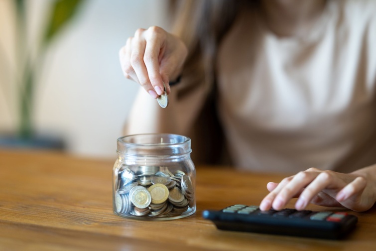Egy nő pénzt gyűjt egy üvegbe, mellette számológép