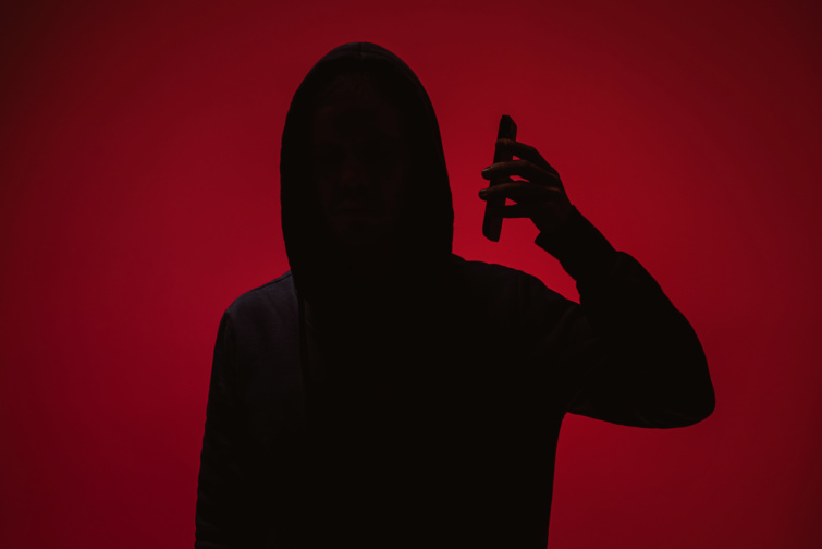 Telefonos csaló sziluettje piros háttér előtt