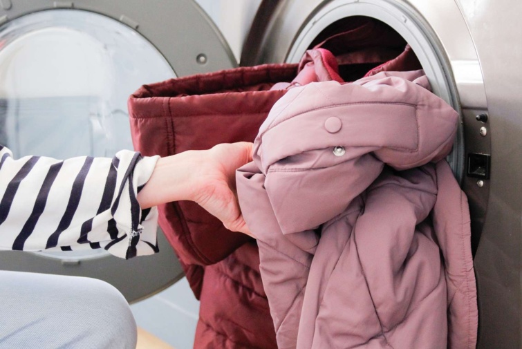 Tollkabátokat mosógépbe rakó női kéz