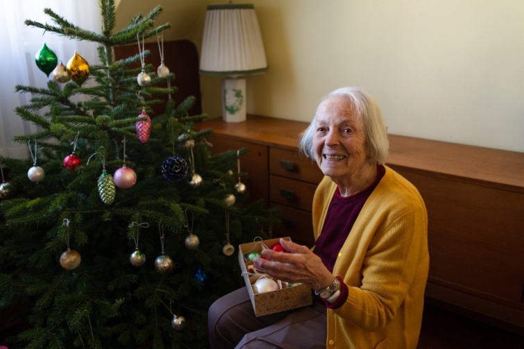 Idős hölgy karácsonyfát díszít