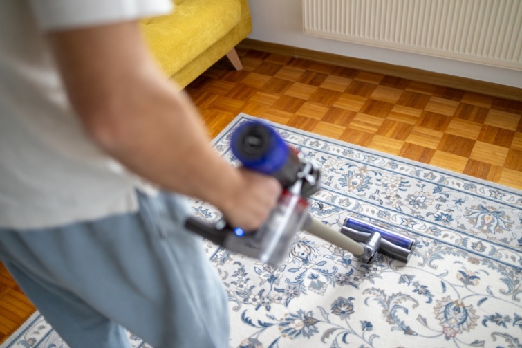 Férfi szőnyeget takarít rúdporszívóval
