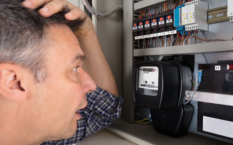 Egy fejét fogó férfi a villanyórát nézi.