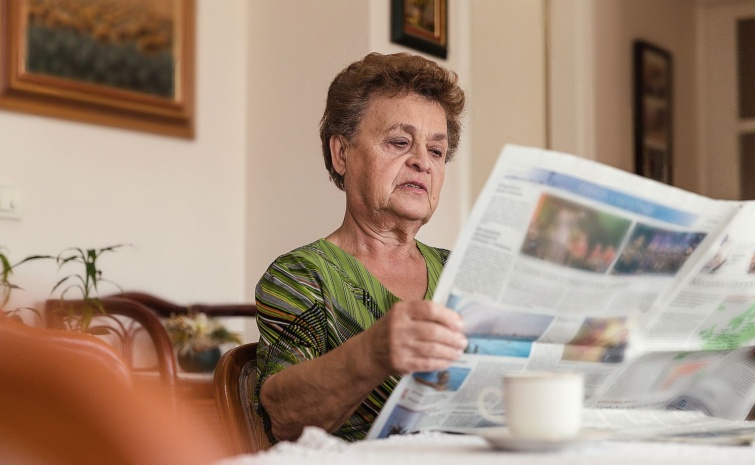 Serious elderly woman reading newspapers Startlap Vásárlás Idős nő újságot olvas a lakásában.