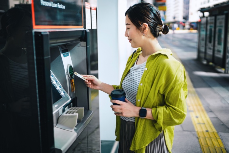 Young Asian woman inserting bank card into automatic cash machine in city street Withdraw money pay bills check account balances and make a bank transfer Personal banking Privacy protection Mobile banking security concept Smart banking on the go Startlap Vásárlás Fiatal nő készpénzt vesz fel egy bankautomatából