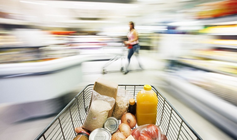 Supermarket trolley races through store with motion blur Startlap Vásárlás Bevásárlókocsi telepakolva elmosódó bolti háttérrel és vásárlóval.