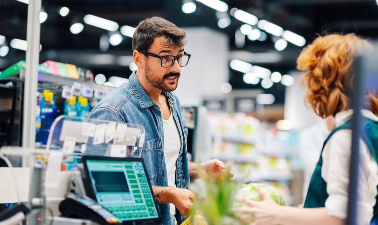 Egy szemüveges férfi a kasszással beszélget a boltban.