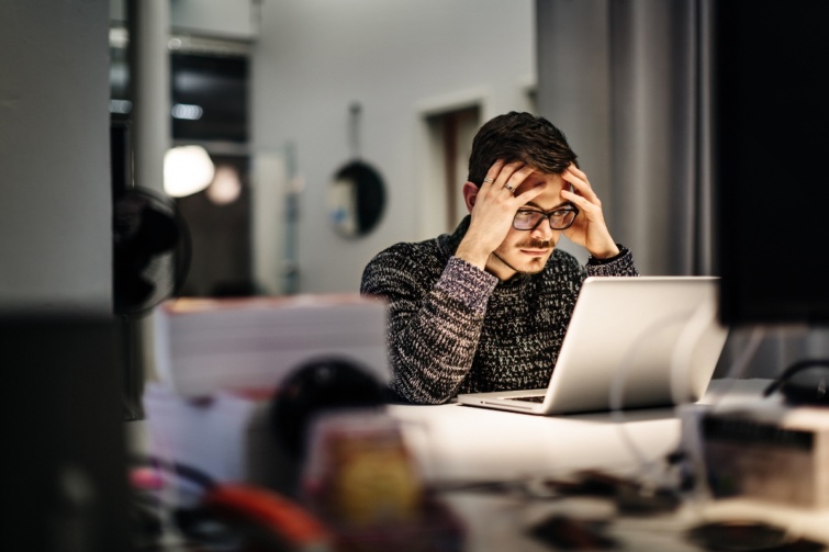 Fiatal szemüveges férfi egy laptop előtt ül