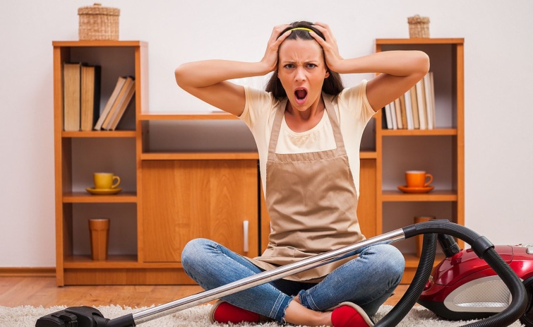 Egy, a porszívó mellett a földön ülő mérges nő a fejét fogva kiabál.