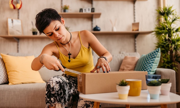 Egy fiatal nő ollóval felbont egy csomagot.