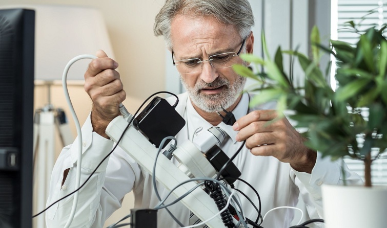 Egy idős szemüveges férfi elosztóba dugott összegabalyodott kábelekkel küzd.