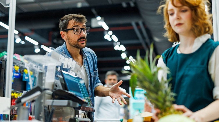 Customer complaining to cashier at supermarket checkout Startlap Vásárlás Egy férfi vásárló magyaráz ingerülten a kasszásnőnek.