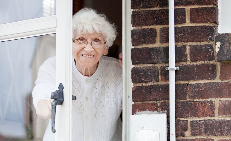 Egy idős nő áll a nyitott ajtóban.