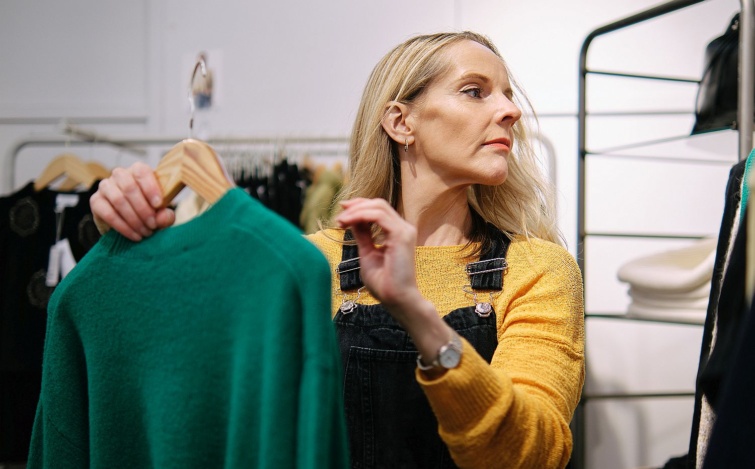 Egy nő egy zöld pulóvert tart a kezében a ruhaboltban.