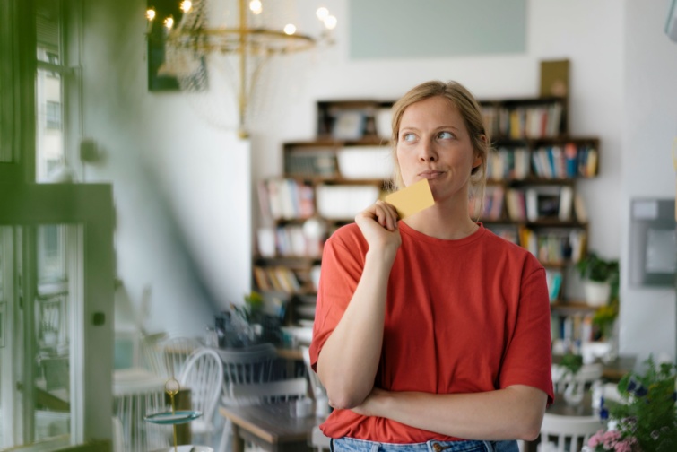 Fiatal nő kezében bankkártyával gondolkodik.