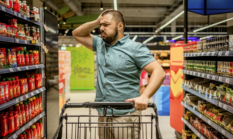 Man feeling upset about the increase in food prices Startlap Vásárlás Egy bevásárlókocsit fogó, fejét vakaró férfi tanácstalanul áll a bolti kínálat előtt