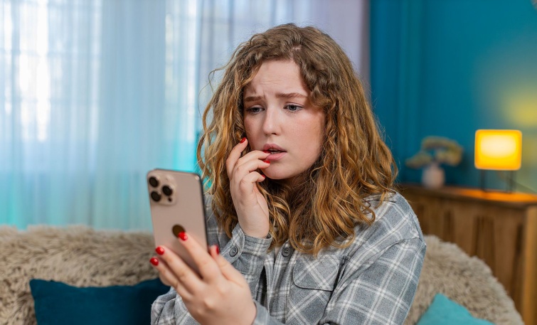 Egy fiatal nő aggódva figyeli a mobiltelefonja kijelzőjét.