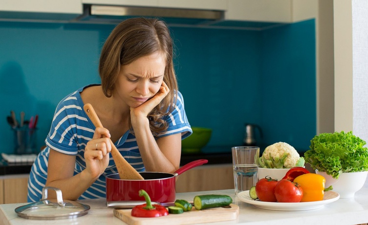 Fiatal nő unottan keverget valamit egy lábasban a konyhában