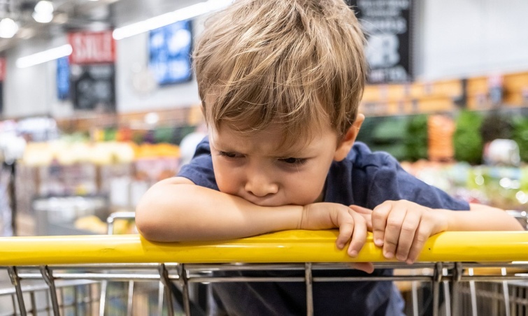 Egy duzzogó kisfiú a bevásárlókocsiban ül a boltban.