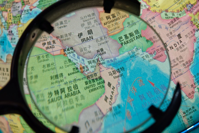 Világtérkép nagyító alatt, Iránra és a Hormuzi-szorosra fókuszálva.