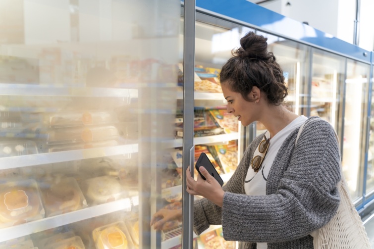Fiatal nő egy mélyhűtőnél válogat az áruk között