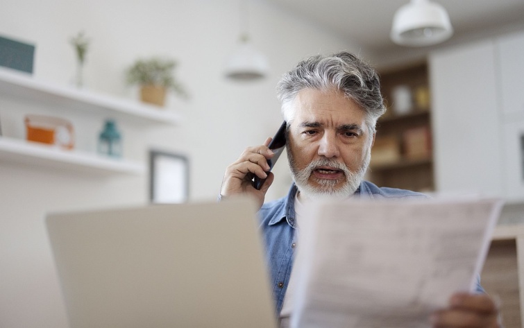 Középkorú férfi mobiltelefonon beszél és egy papírlapot tart a másik kezében.