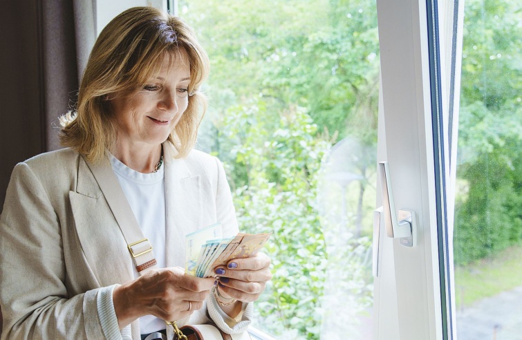 Egy ebalkban álló, mosolygó középkorú nő bankjegyeket számol.