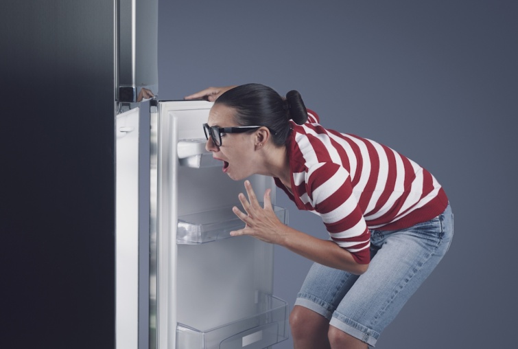 Disappointed hungry woman and empty fridge Startlap Vásárlás Fiatal nő áll a hűtő előtt rövid nadrágban, megdöbbenő tekintettel néz a belső térbe.