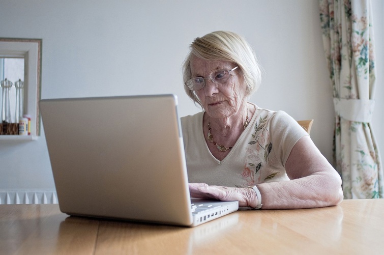 Egy szemüveges idős nő egy laptopot néz.