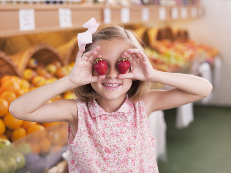 Kislány a szeme előtt tart két szem epret
