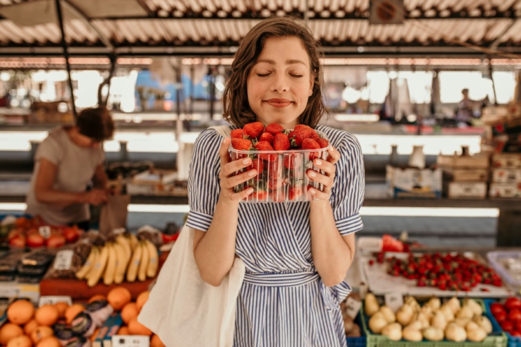 Mosolygó nő csomagolt epret tart a kezében a piacon.