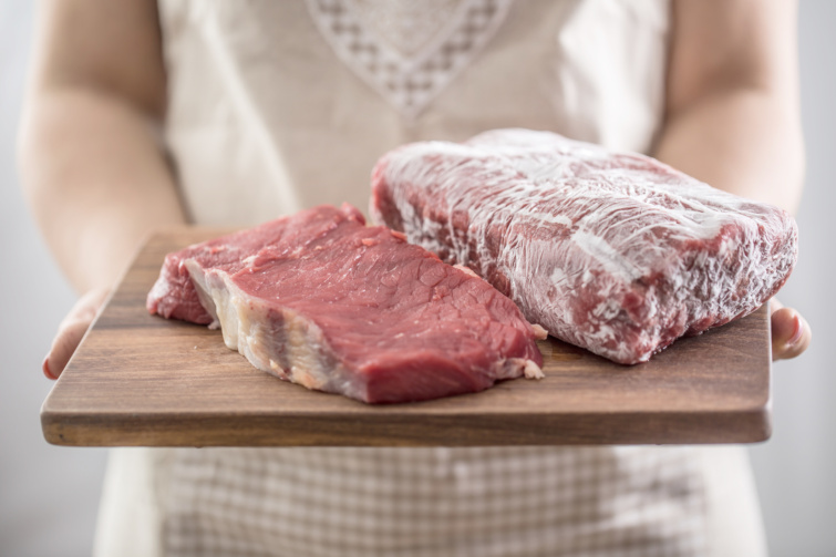 fagyasztott húst vágódeszkán tartó női kéz