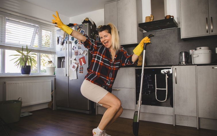 Egy fiatal widám nő takarítás közben viccesen pózol.