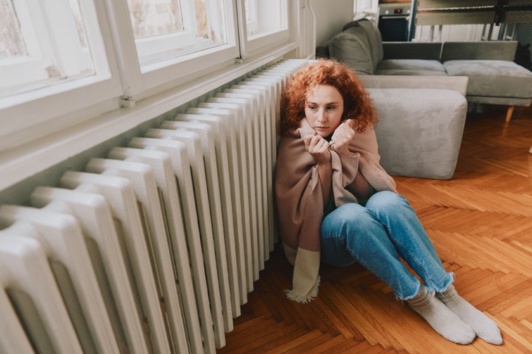 Fázó nő ül a radiátor mellett.