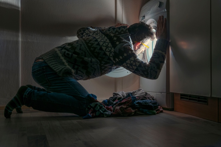 Férfi néz bele a mosógépbe a sötétben.